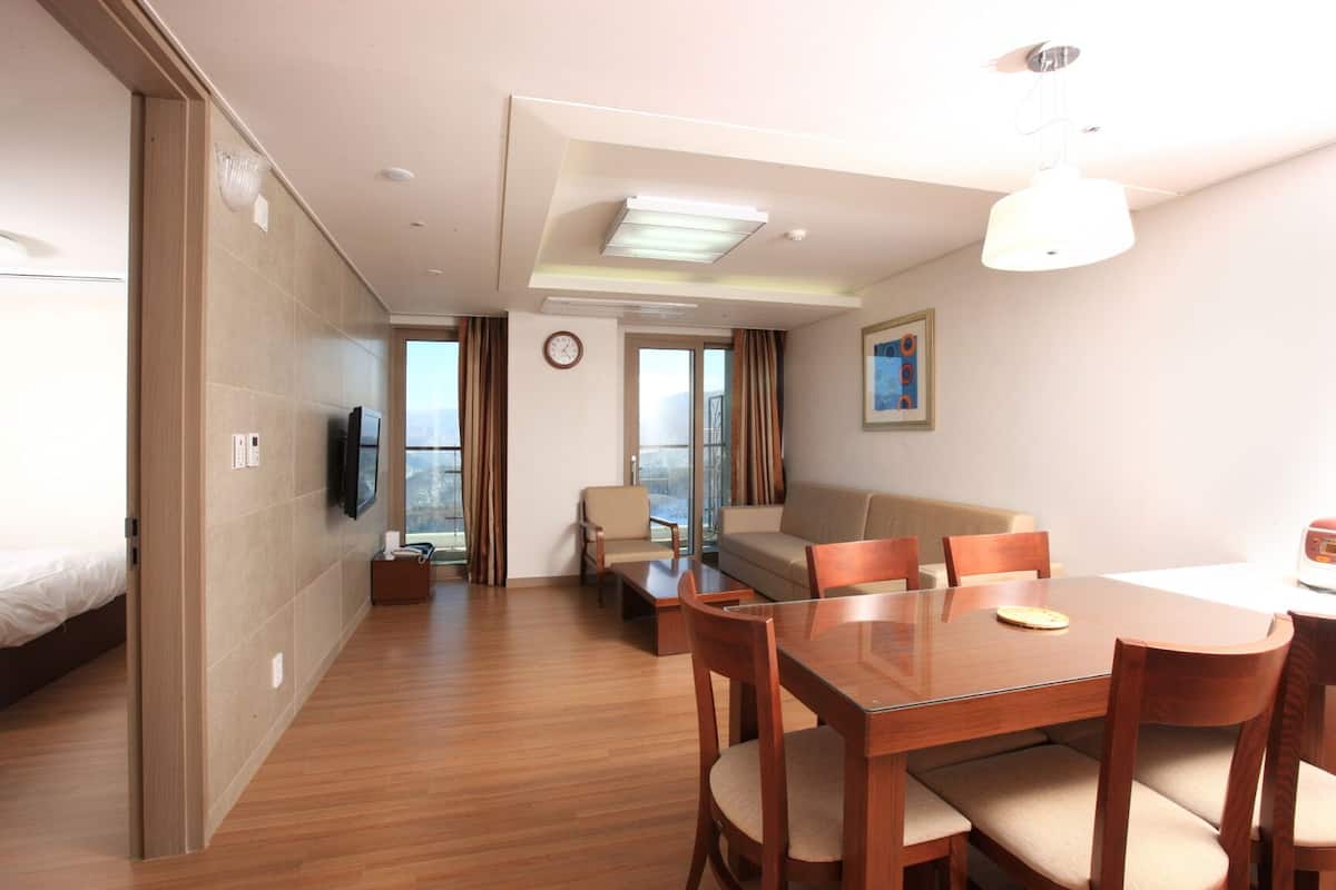 Ein Hotelzimmer mit Bett, Fernseher, Esstisch mit Stühlen, einer Couch und einem großen Fenster mit Aussicht.
