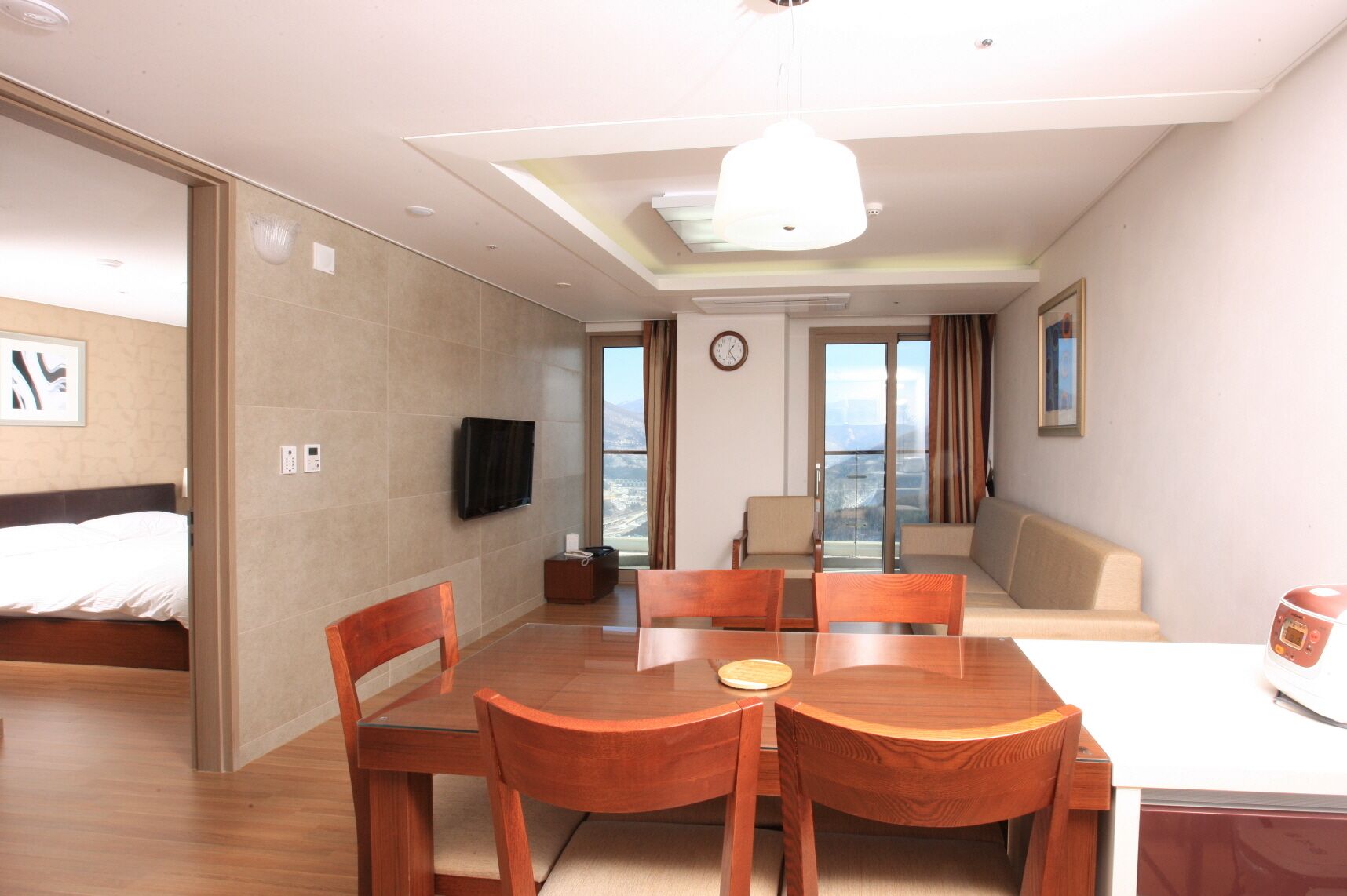 A hotel room with a bed, a TV, a dining table with chairs, a sofa, and a view of the outdoors.
