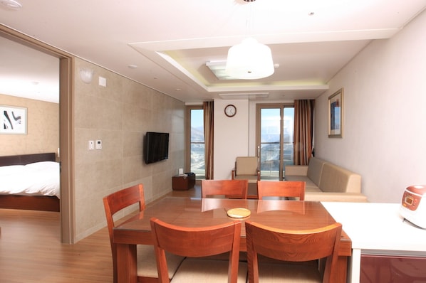 Habitación de hotel con cama, televisor, mesa de comedor con sillas, sofá y vistas al exterior.