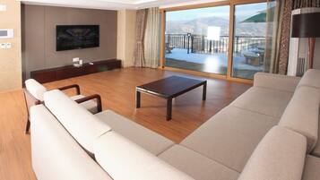 A spacious living room with a large sofa, a coffee table, and a flat-screen TV mounted on the wall.