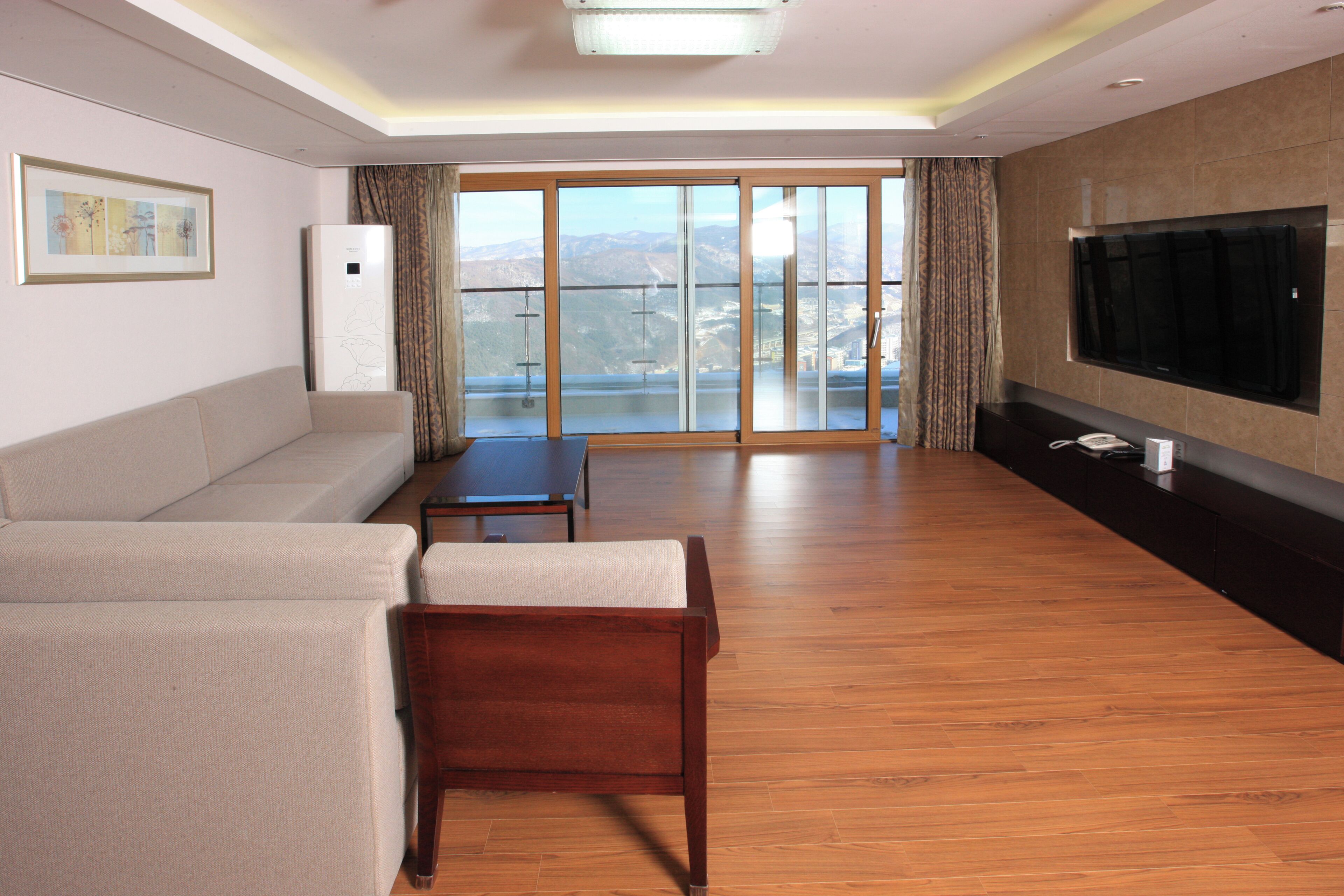 A modern living room with a sofa, a wooden chair, a TV, and a balcony with a view.