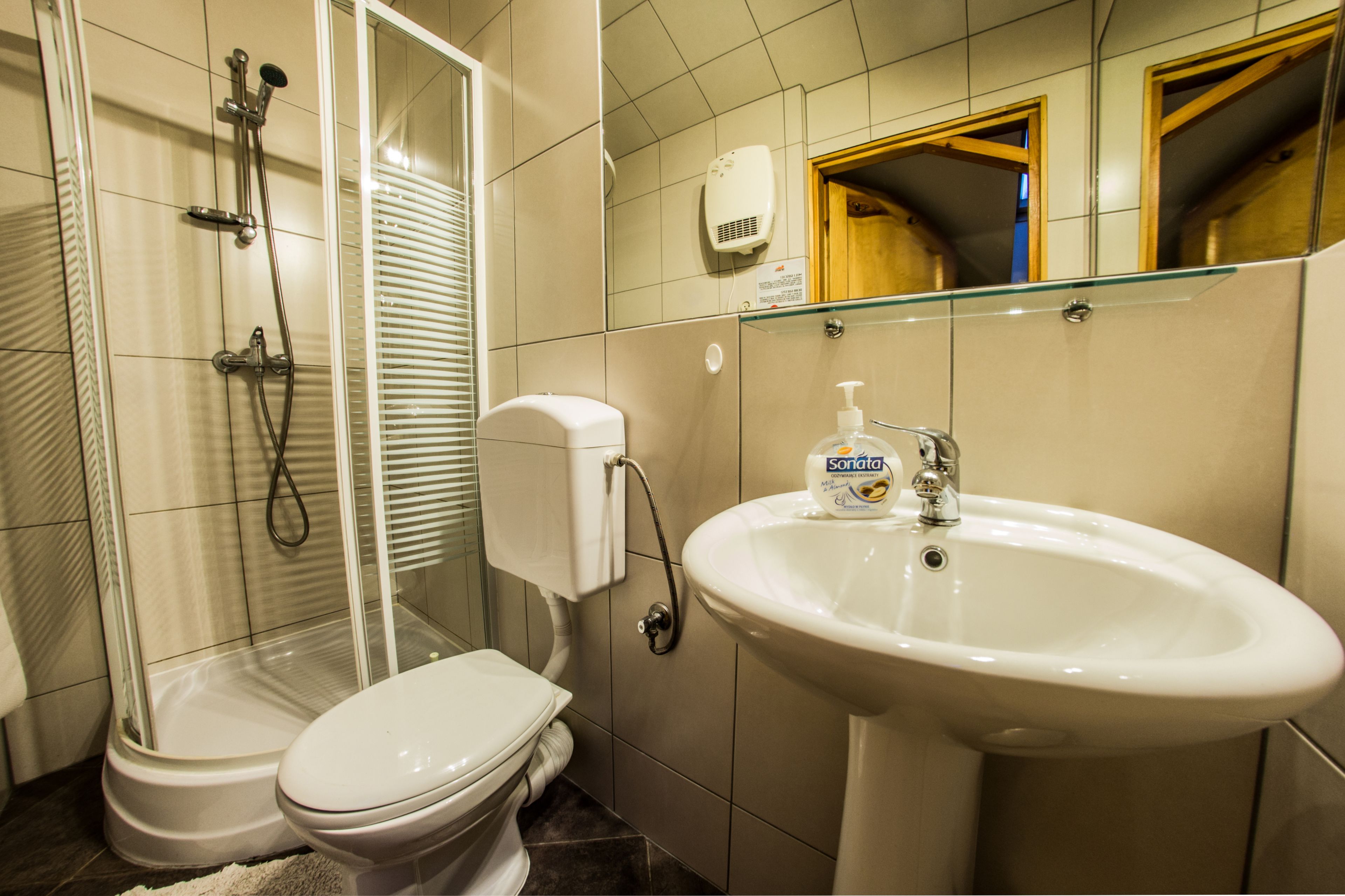 Un baño con inodoro, ducha con mampara de vidrio, lavamanos y dispensador de jabón.