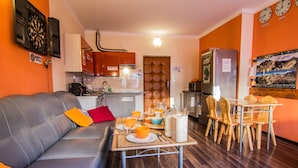 A modern living room with a grey sofa, dining table, and chairs. A kitchen is visible in the background with a refrigerator and microwave. - Top Hostel (Zakopane)
