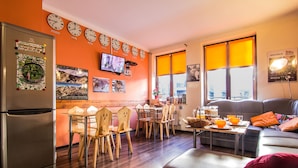 A modern kitchen with a refrigerator, wooden chairs, a dining table, and a TV mounted on the wall. - Top Hostel (Zakopane)