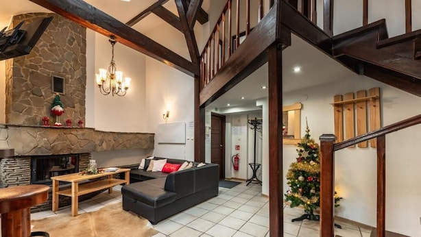 A spacious living area with a stone fireplace, a black sofa, a wooden coffee table, and a Christmas tree. - Top Hostel (Zakopane)