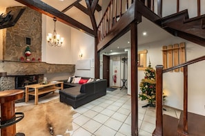 A spacious living area with a stone fireplace, a black sofa, a wooden coffee table, and a Christmas tree. - Top Hostel (Zakopane)