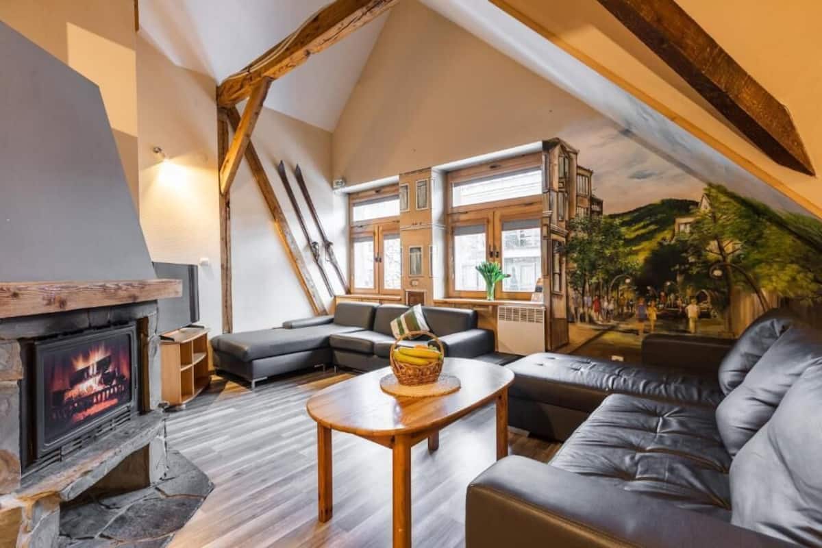 Ett vardagsrum i loftstil med en öppen spis, lädersoffor och ett stort fönster med utsikt över en gata.