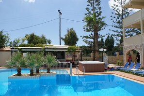 A swimming pool with lounge chairs, a hot tub, and a building with a balcony. - Sunny Suites (Platanias)