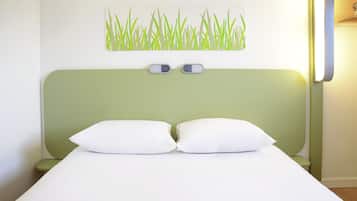 A bed with a green headboard, two white pillows, and a wall-mounted light fixture.