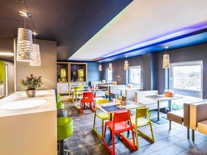 Interior moderno de restaurante con varias mesas, sillas coloridas e iluminación colgante.