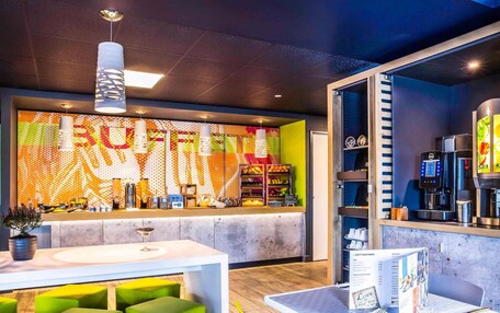 A modern cafe with a colorful wall mural, a coffee machine, and green seating.