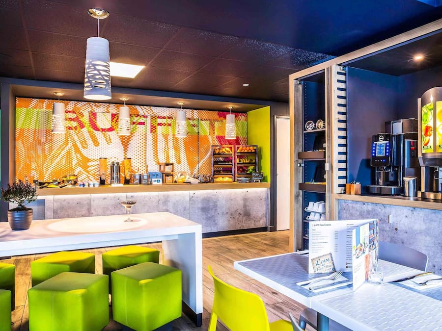 A modern cafe with a colorful wall mural, a coffee machine, and green seating.