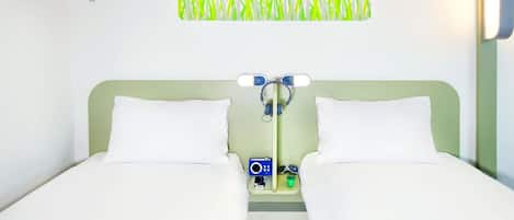 A double bed with white bedding, a small bedside table with a clock and a pair of sunglasses, and a wall-mounted towel rack.