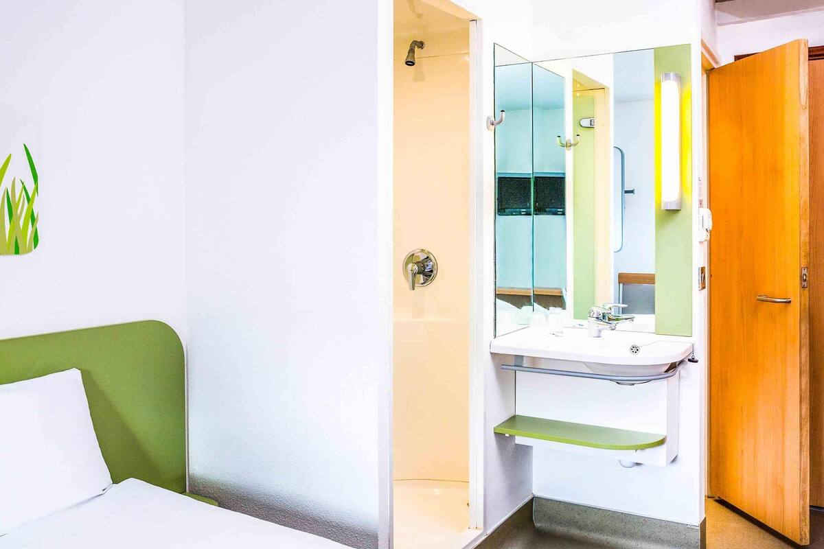 A hotel room with a bed, a green headboard, a bathroom with a sink, mirror, and shower.