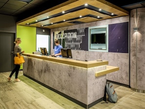A reception desk with a wooden counter, a large window, and a wall with a graphic design. - ibis budget Glasgow (Glasgow)