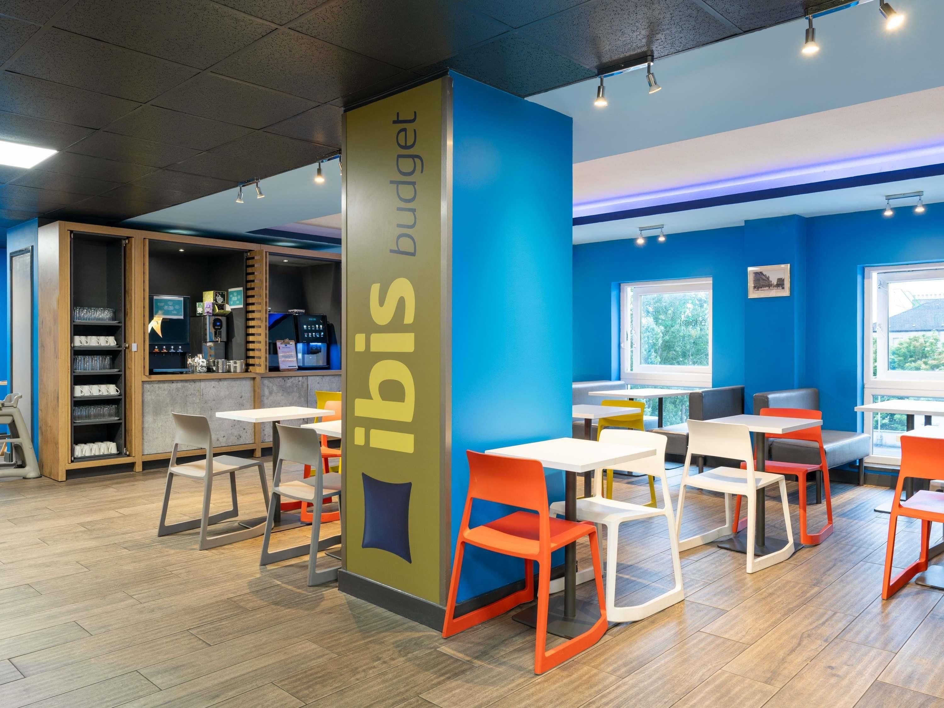 A modern interior with a blue accent wall, a column labeled 'ibis budget,' and a seating area with tables and chairs.