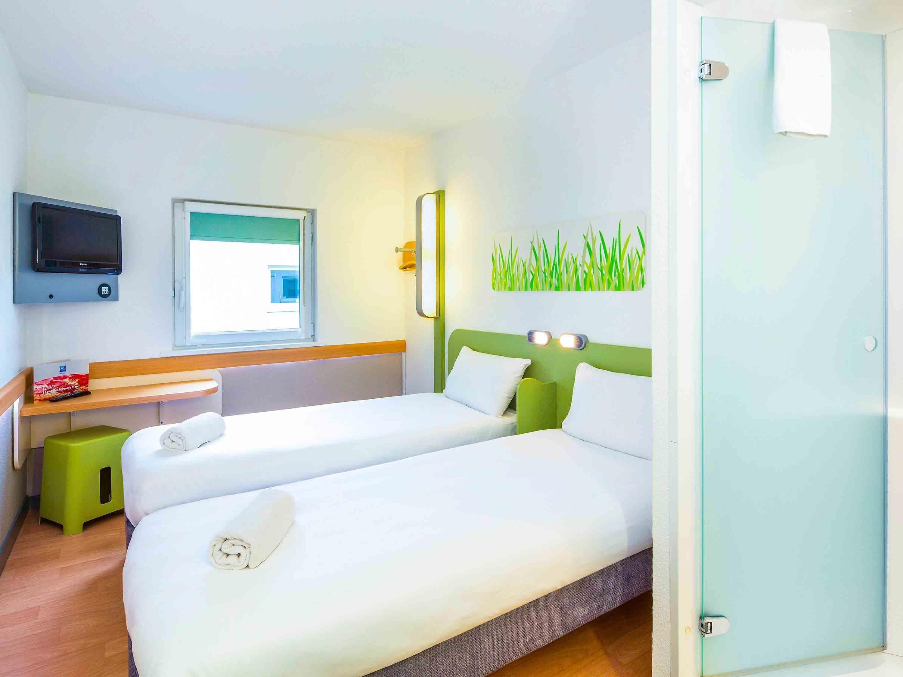 A hotel room with two beds, a TV, a window, and a green wall decoration.