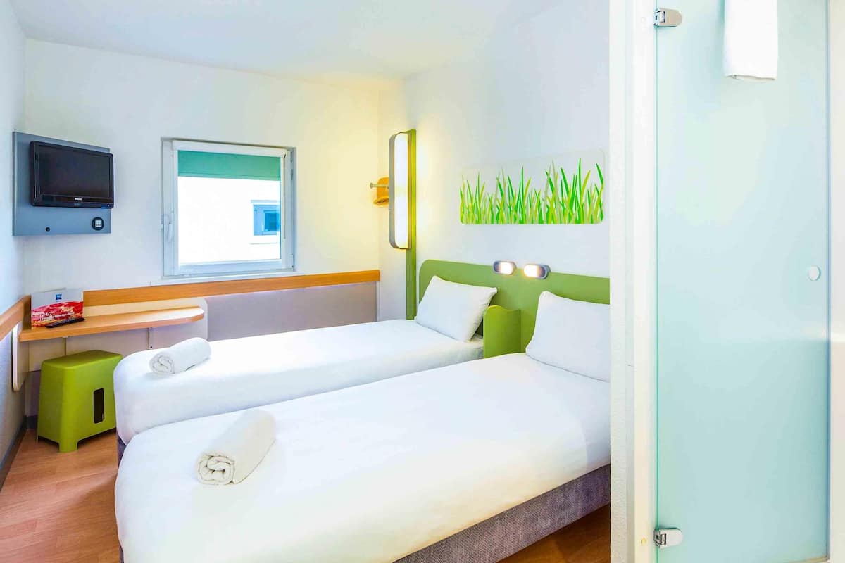 A hotel room with two beds, a TV, a window, and a green wall decoration.