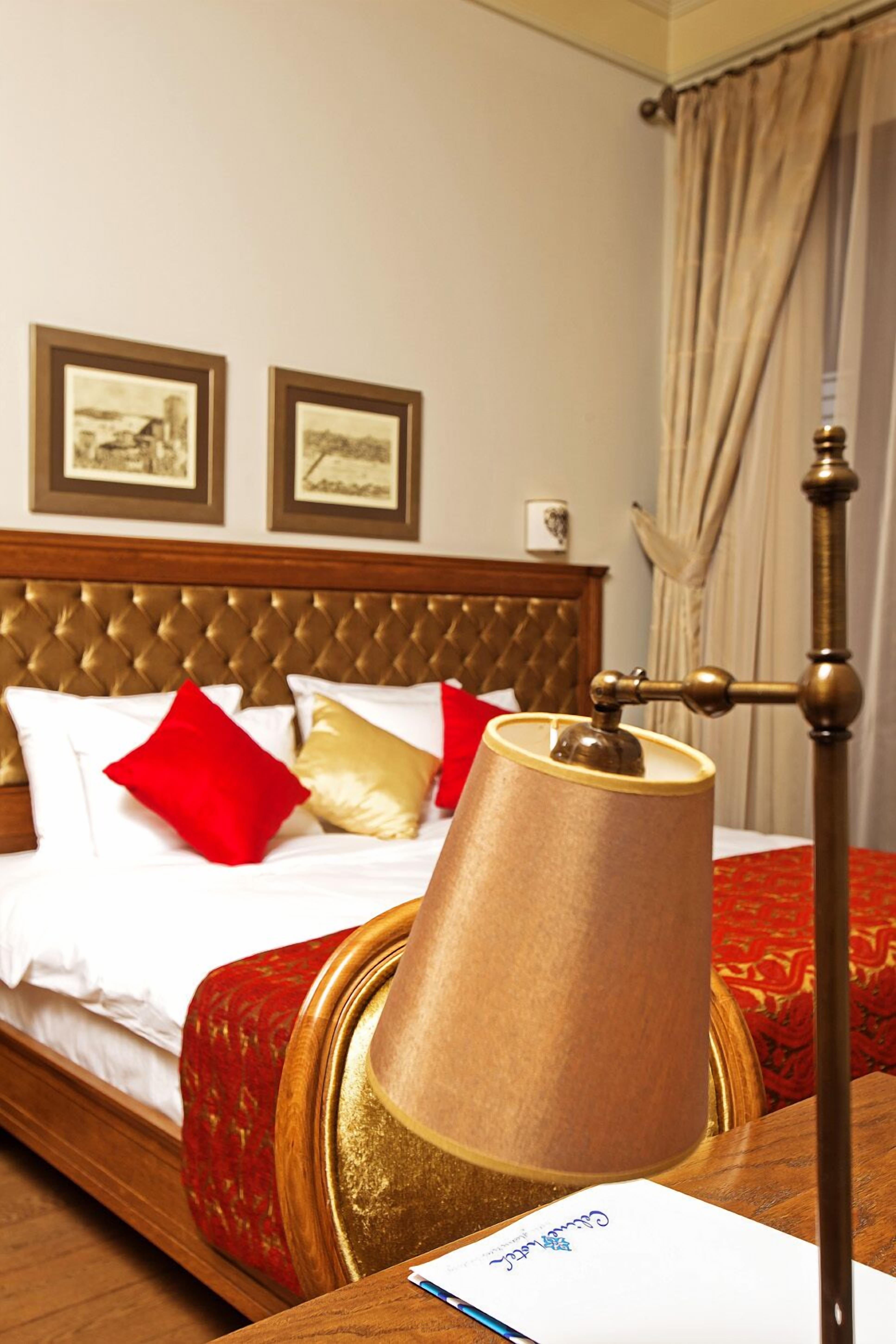 A hotel room with a bed, a lamp, and two framed pictures on the wall.
