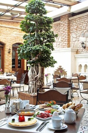 A dining area with a table set for breakfast, a large tree, and stone walls. - Celine Hotel (Istanbul)
