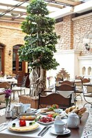 Zona pranzo con tavolo apparecchiato per la colazione, un grande albero e pareti in pietra.