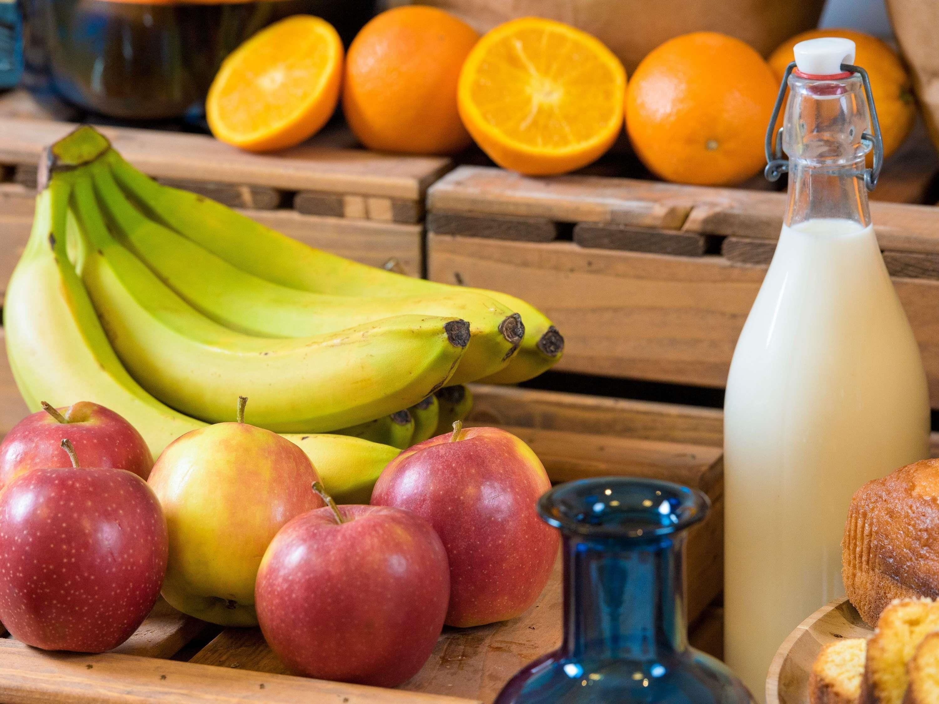 A wooden table with fruits, a milk bottle, and a blue glass bottle.
