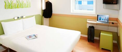 Ein Hotelzimmer mit einem Bett, einem Schreibtisch mit einem Laptop, einem Fernseher und einem Fenster.