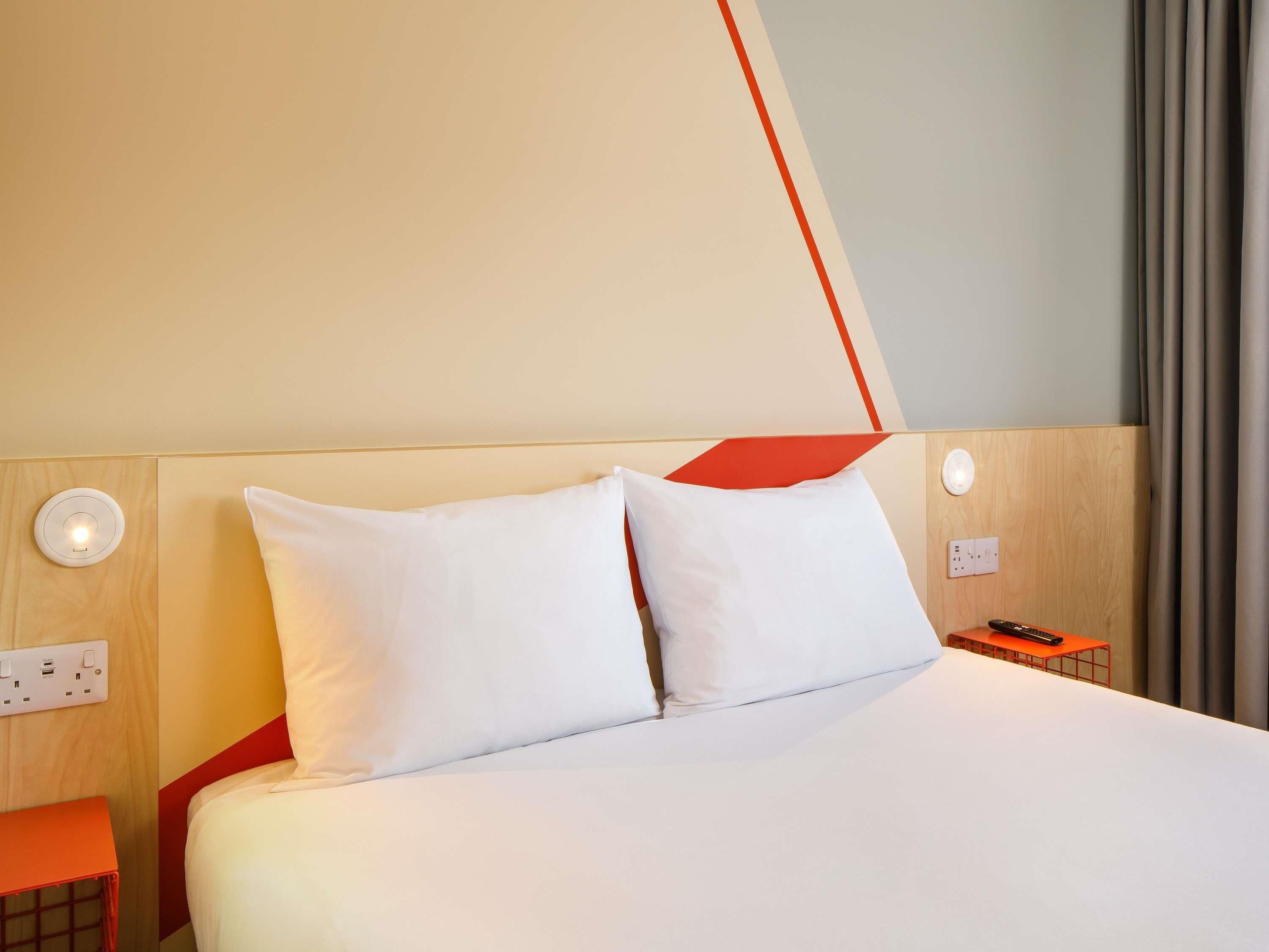 Une chambre d’hôtel comprenant un lit, deux tables de chevet, une lampe fixée au mur et une prise de courant.