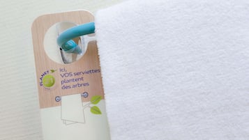 Una etiqueta unida a una toalla blanca, con fondo de madera y un asa azul.