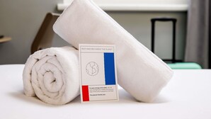 A neatly folded white towel and a card on a bed with a window in the background.