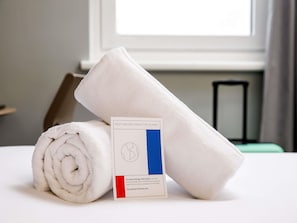 A neatly folded white towel and a card on a bed with a window in the background. - ibis budget Birmingham Centre (Birmingham)