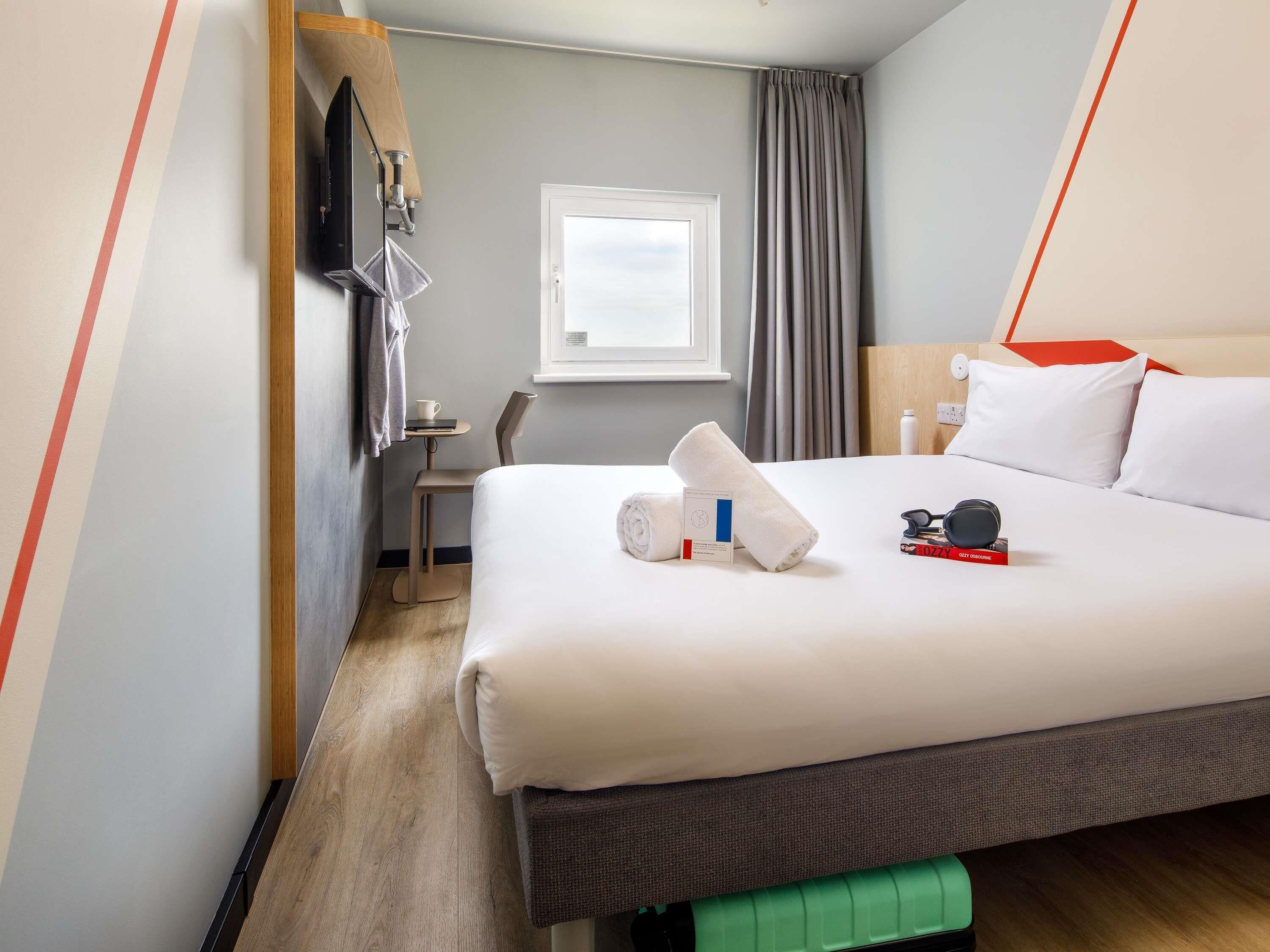 Hotelkamer met een bed, bureau, stoel, raam en een aan de muur bevestigde televisie.