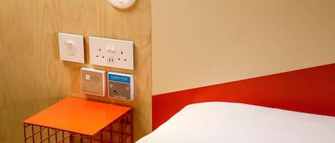 Habitación de hotel con cama, una mesita pequeña y un sistema de alarma instalado en la pared.