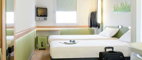 A hotel room with two beds, a television, a window, a desk, a mirror, and a suitcase.