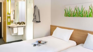 A hotel room with a bed, a bedside table, a mirror, a bathroom with a sink, and a towel rack.