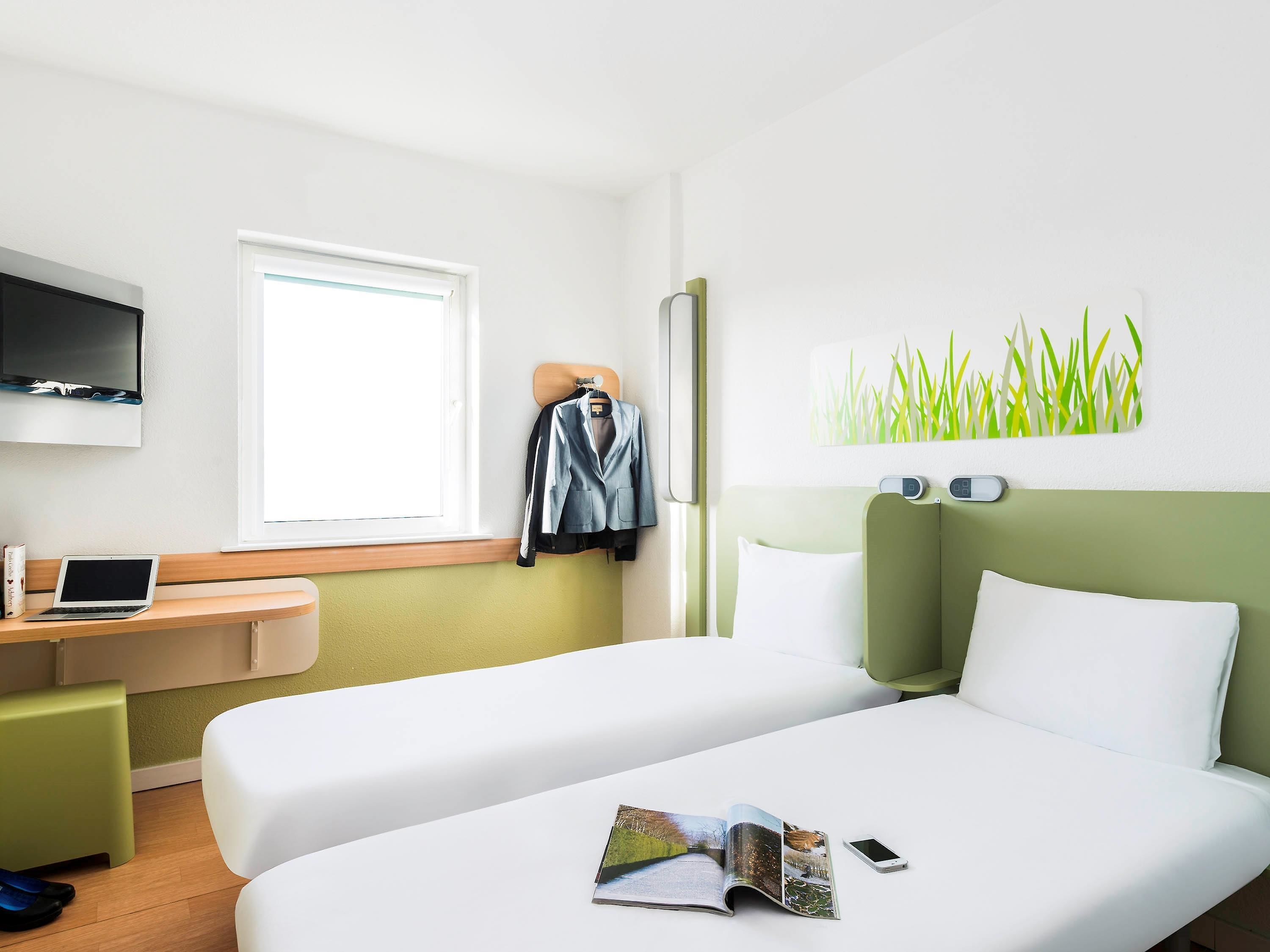 A hotel room with a bed, a desk with a laptop, a TV, and a window.