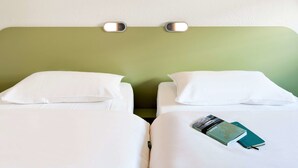 Habitación de hotel con dos camas, ropa blanca, cabecera verde y una lámpara fijada a la pared.