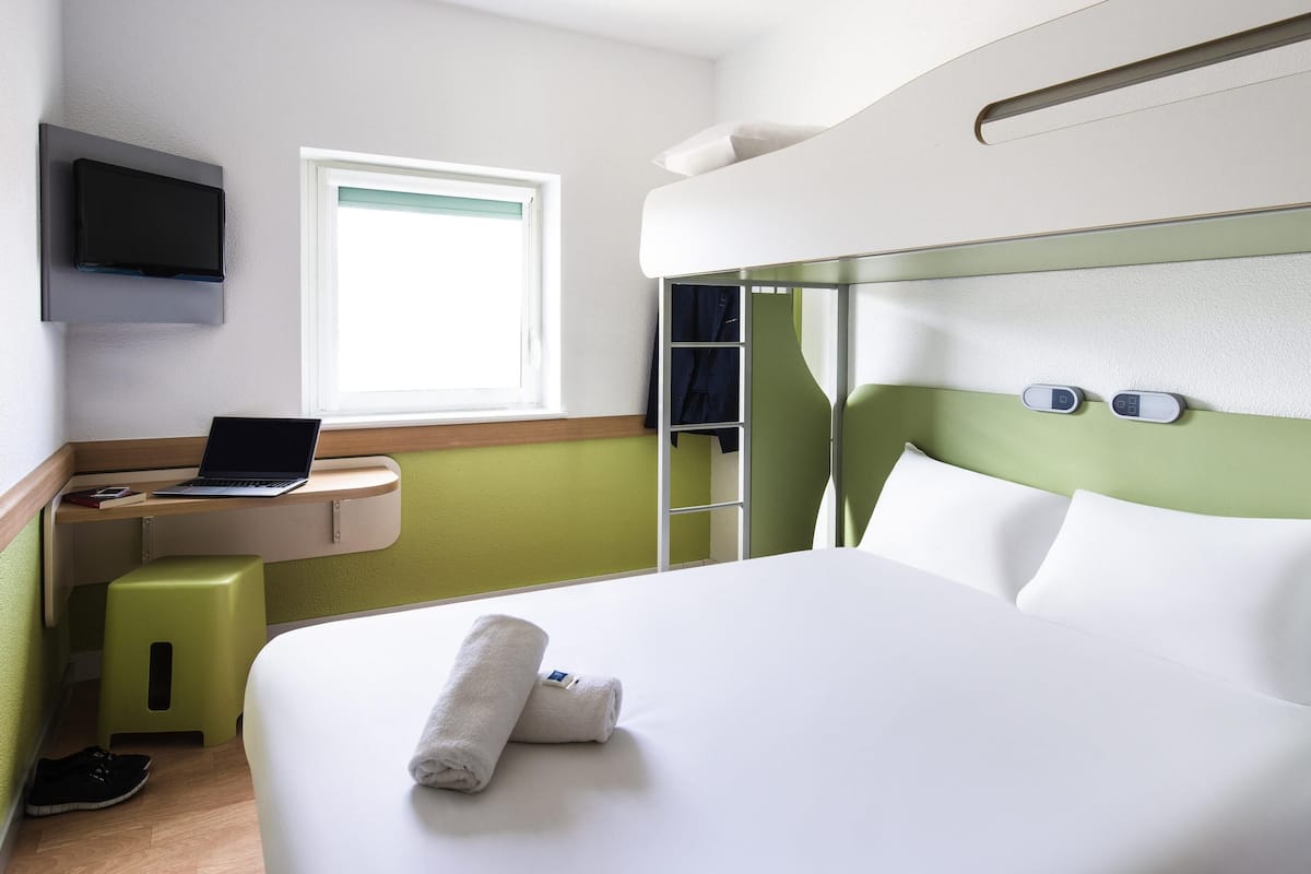 Habitación de hotel con cama, escritorio con computadora portátil, televisor montado en la pared y ventana.