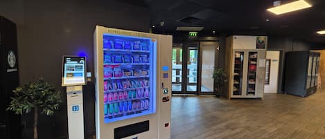 Un distributeur automatique proposant une variété de collations et de boissons, une enseigne Starbucks et une plante.