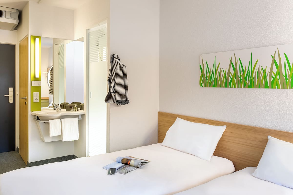Habitación de hotel con cama, mesita de noche, espejo, lavabo y toallero.