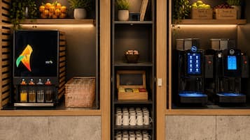 L’intérieur d’un café, avec une machine à café, un présentoir de fruits et une étagère remplie de tasses.