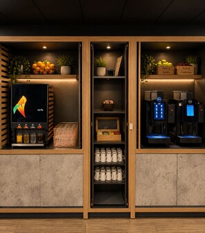 Interior de una cafetería con una máquina de café, una exposición de frutas y una estantería con tazas.