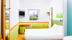 Quarto de hotel com cama, escrivaninha, televisão, janela e vista para a cidade, além de banheiro.