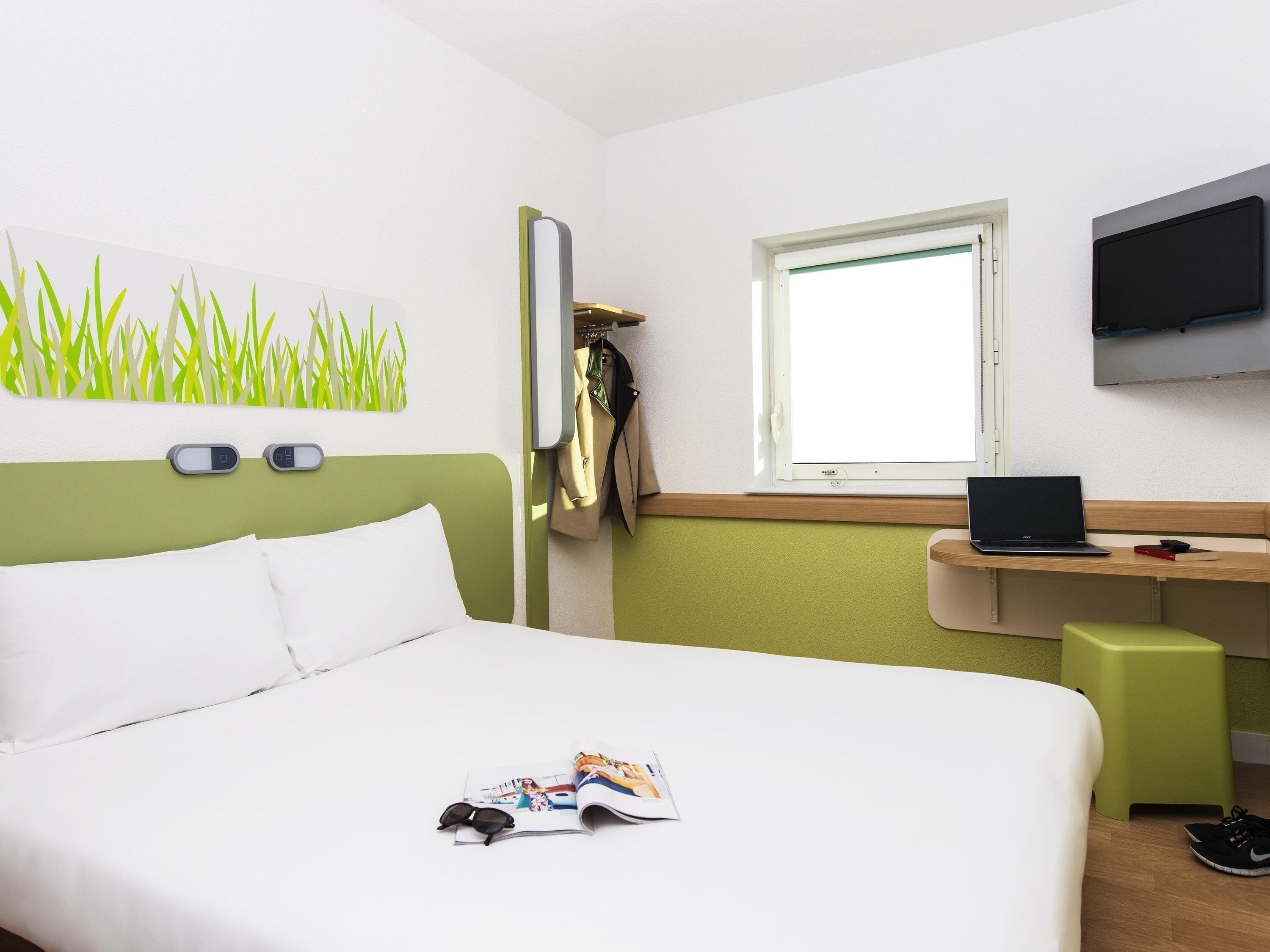 Une chambre d’hôtel avec un lit, un bureau, un ordinateur portable et une télévision.