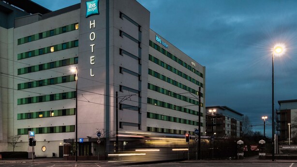 Um hotel moderno com um destaque para o letreiro 'ibis budget', vários andares e uma entrada visível.