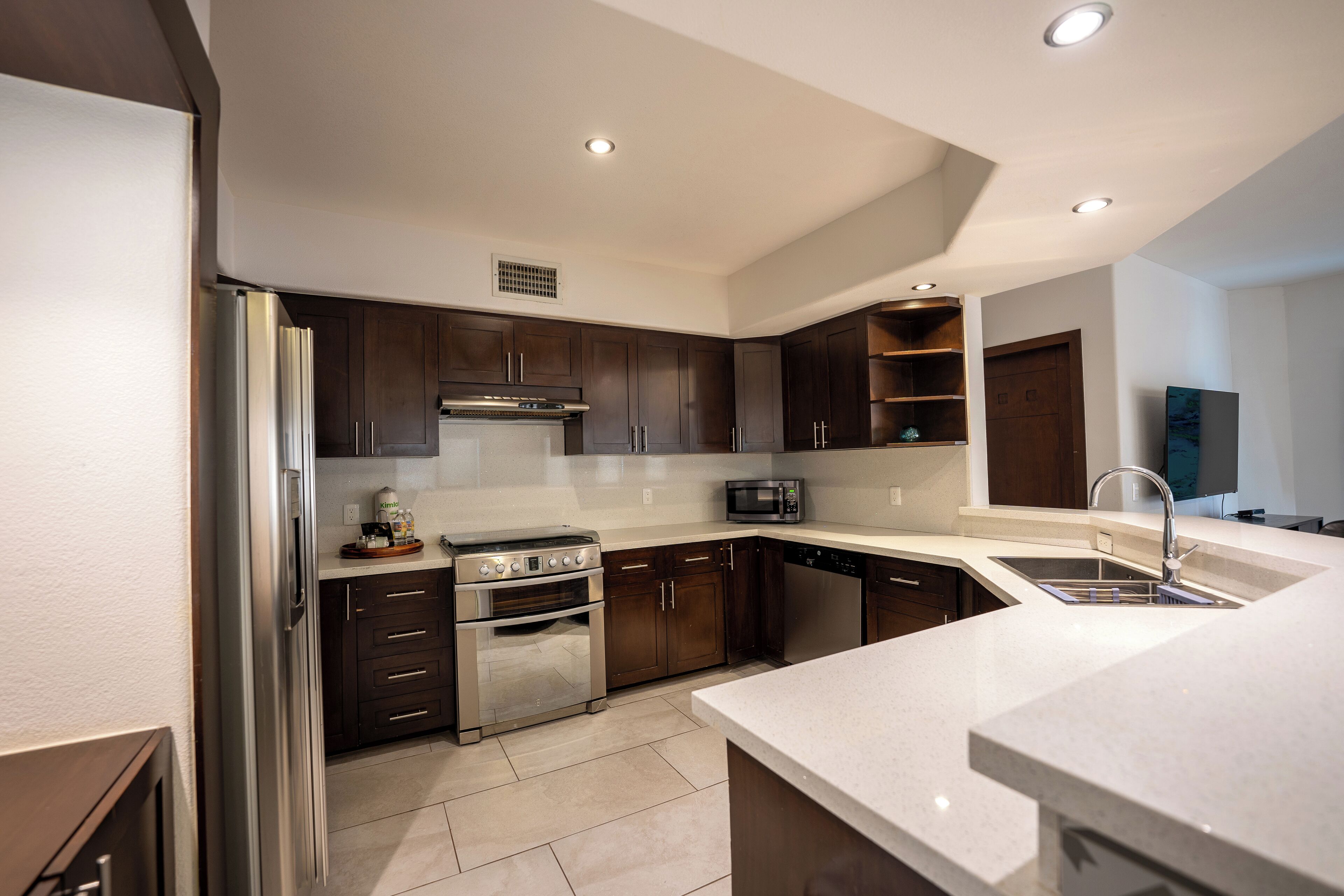 A modern kitchen with stainless steel appliances, dark wood cabinets, and a white countertop.
