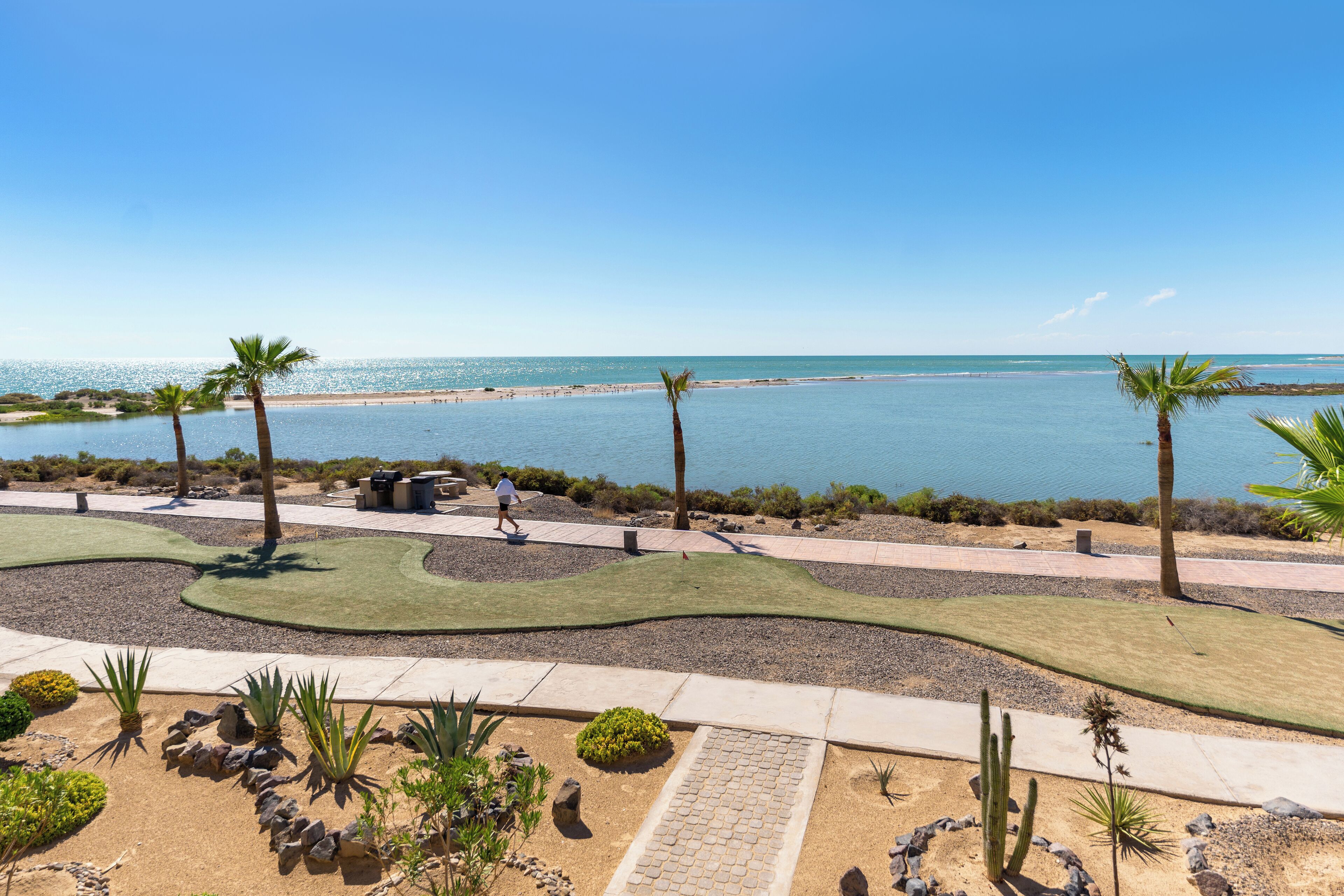 Un espace aménagé avec un sentier, des palmiers et une vue sur la plage et l’océan.