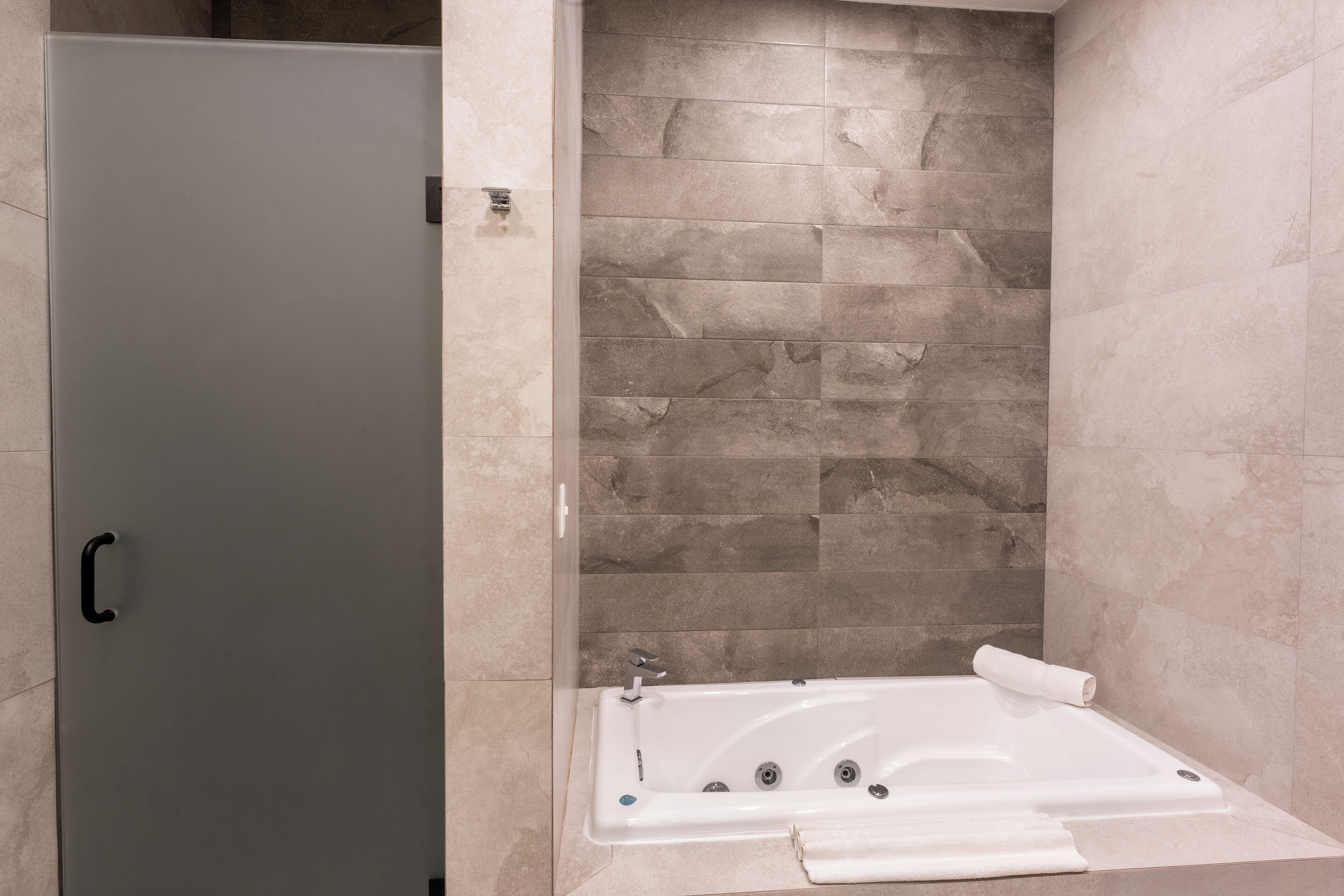 Een badkamer met een glazen deur, een vrijstaand bad en een betegelde muur.