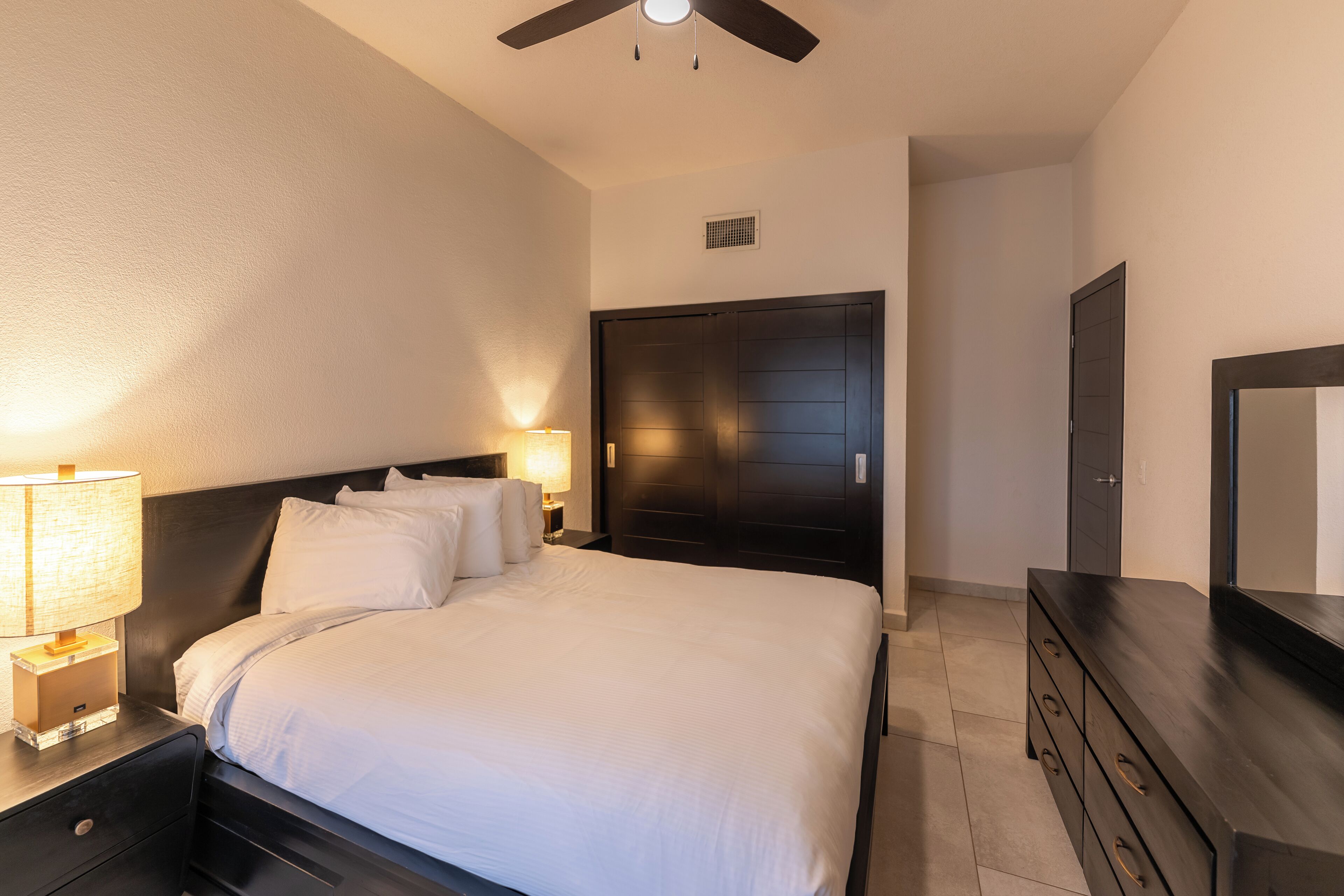 A neatly made bed with white linens, a dark wooden headboard, and a nightstand with a lamp.