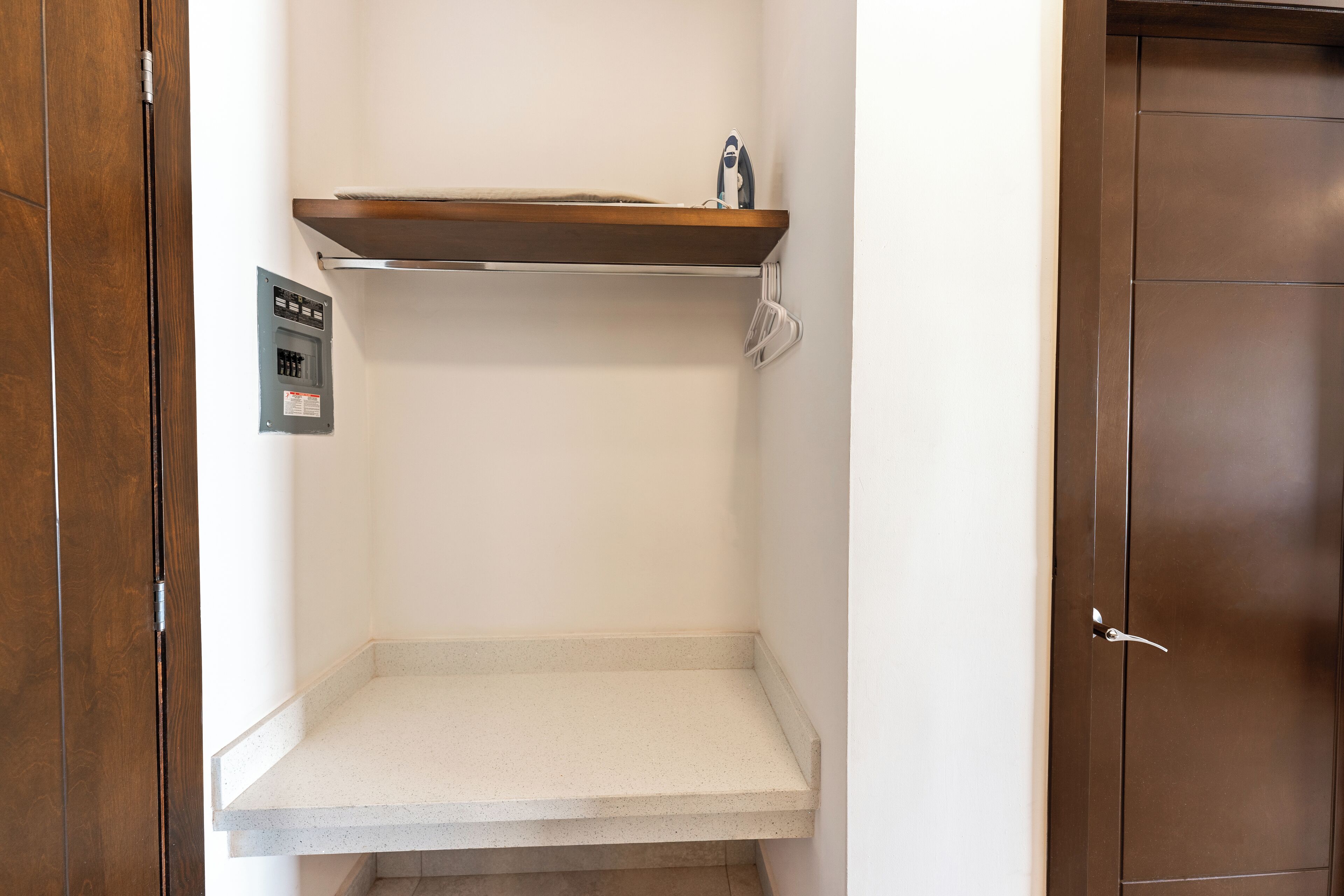 Una stanza con una porta in legno, una parete bianca, uno scaffale in legno con un asciugamano e un quadro elettrico bianco.